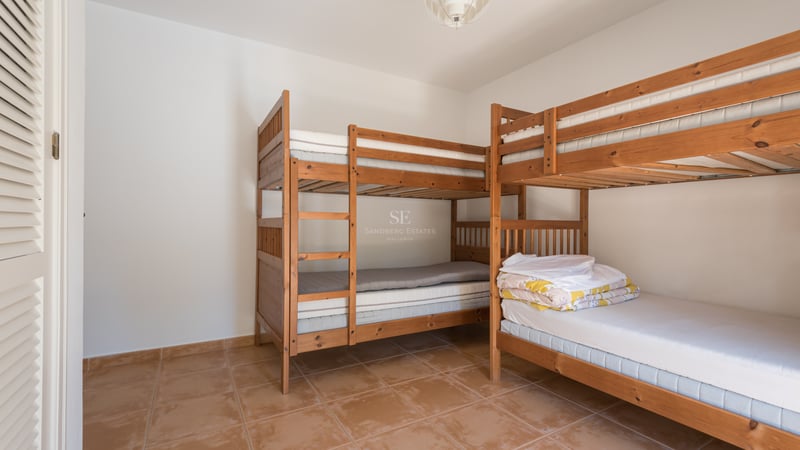 Une chambre lumineuse avec deux lits superposés en bois et un sol en terre cuite.
