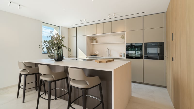 Cuisine moderne minimaliste avec un grand îlot central, des tabourets design et des armoires lisses aux tons terreux.