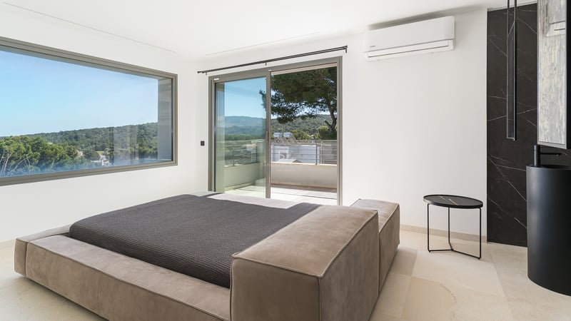 Chambre moderne avec lit bas, grandes baies vitrées coulissantes ouvrant sur une terrasse et vue sur les collines.