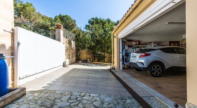 Voiture garée dans un garage spacieux à côté d'une allée en pierre naturelle avec un grand portail coulissant blanc.