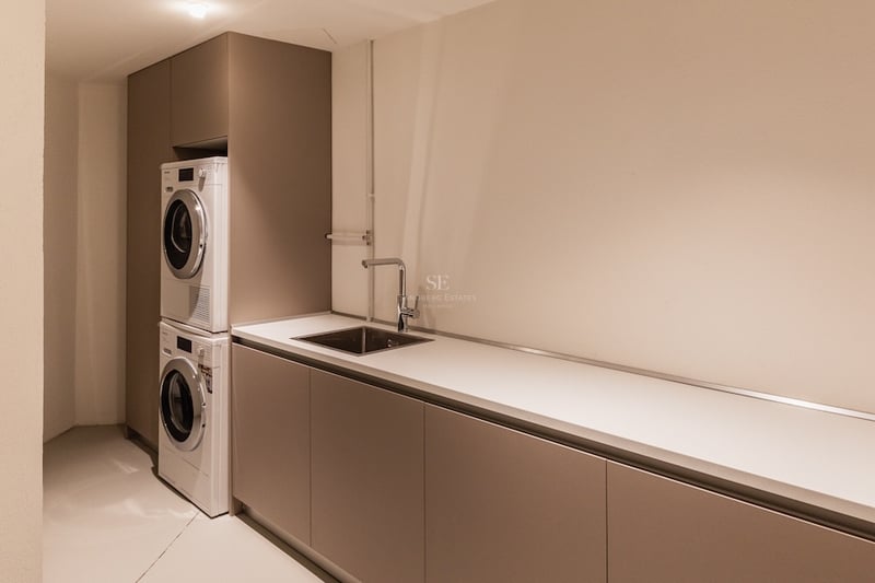 Buanderie moderne avec lave-linge et sèche-linge superposés, plan de travail blanc et évier en inox.