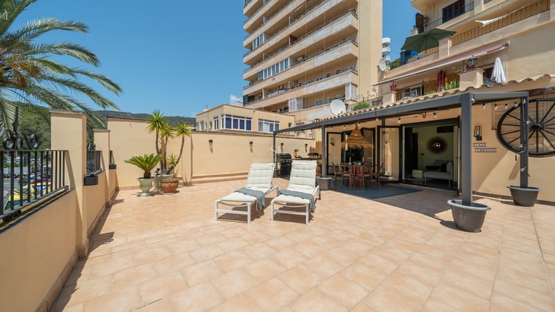 Grande terrasse avec carrelage en terre cuite, deux chaises longues blanches et un coin repas ombragé sous une pergola.