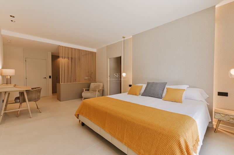 Chambre moderne avec grand lit, jeté de lit jaune et cloison en lattes de bois verticales dans des tons neutres.