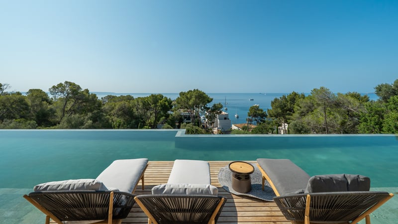 Trois chaises longues modernes sur une terrasse en bois surplombant une piscine à débordement et la mer.
