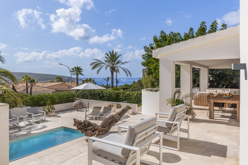 Terrasse ensoleillée avec chaises longues blanches, piscine privée et vue sur la mer sous un ciel bleu.