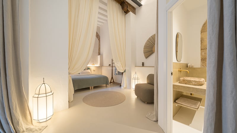 Chambre élégante avec des rideaux fluides, des poutres en bois, des lanternes et une salle de bain avec vasque en pierre.