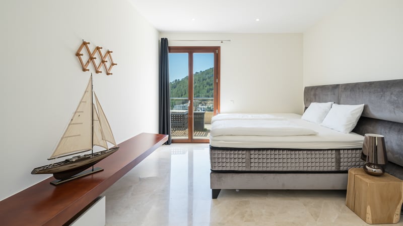 Chambre lumineuse avec sol en marbre, lit en velours gris et porte vitrée offrant une vue sur la montagne.