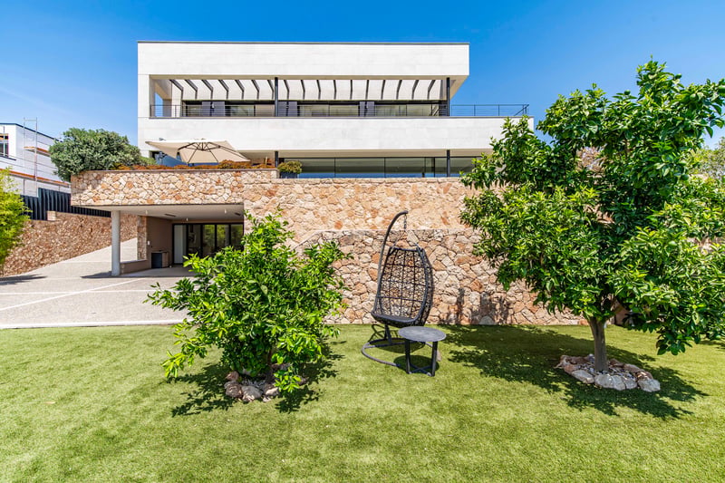 Extérieur d'une villa moderne de trois étages avec murs en pierre, niveaux supérieurs blancs et jardin paysager.