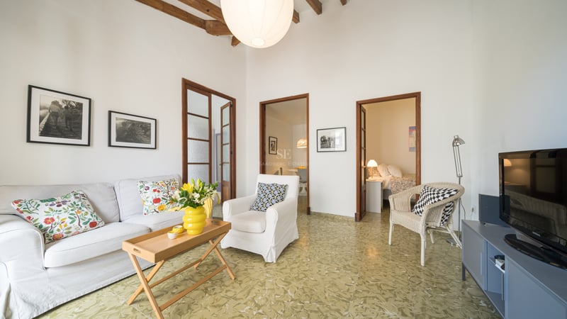 Salon lumineux avec canapé blanc, poutres en bois rustiques, carrelage vert à motifs et ouvertures vers d'autres pièces.