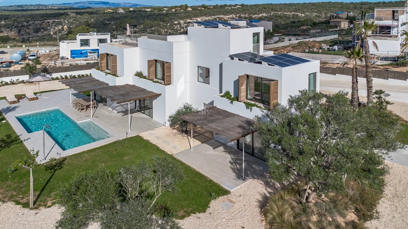 Vue aérienne d'une villa blanche contemporaine avec piscine turquoise, panneaux solaires et jardin paysager.