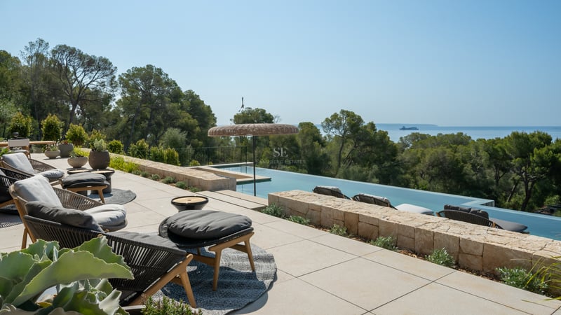 Terrasse de luxe en pierre avec piscine à débordement, salon de jardin design et vue sur la pinède et la mer.