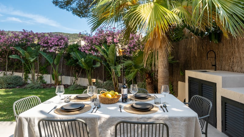 Table à manger extérieure pour six dans un jardin tropical à côté d'une cuisine d'été moderne en pierre.