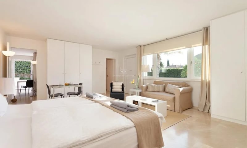 Vaste chambre parentale avec sol en marbre, coin salon, grande fenêtre sur jardin et placards blancs intégrés.