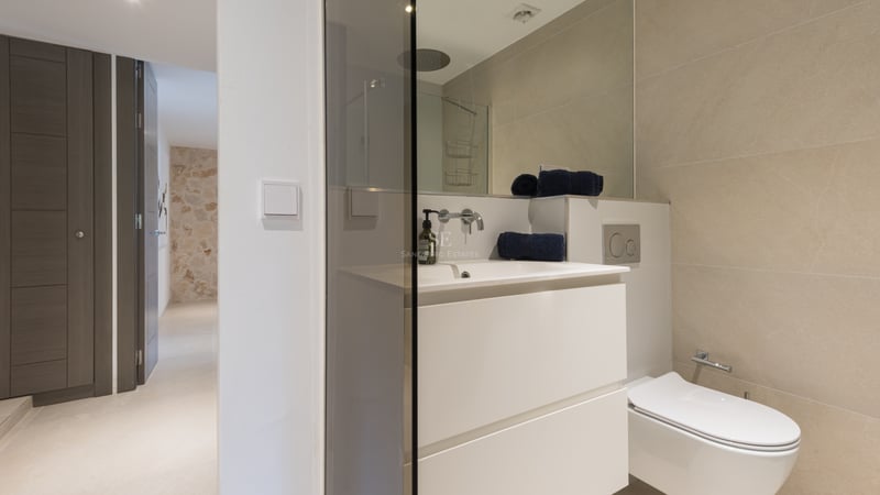 Salle de bains contemporaine avec meuble vasque suspendu blanc, douche vitrée et carrelage grand format ton sable.