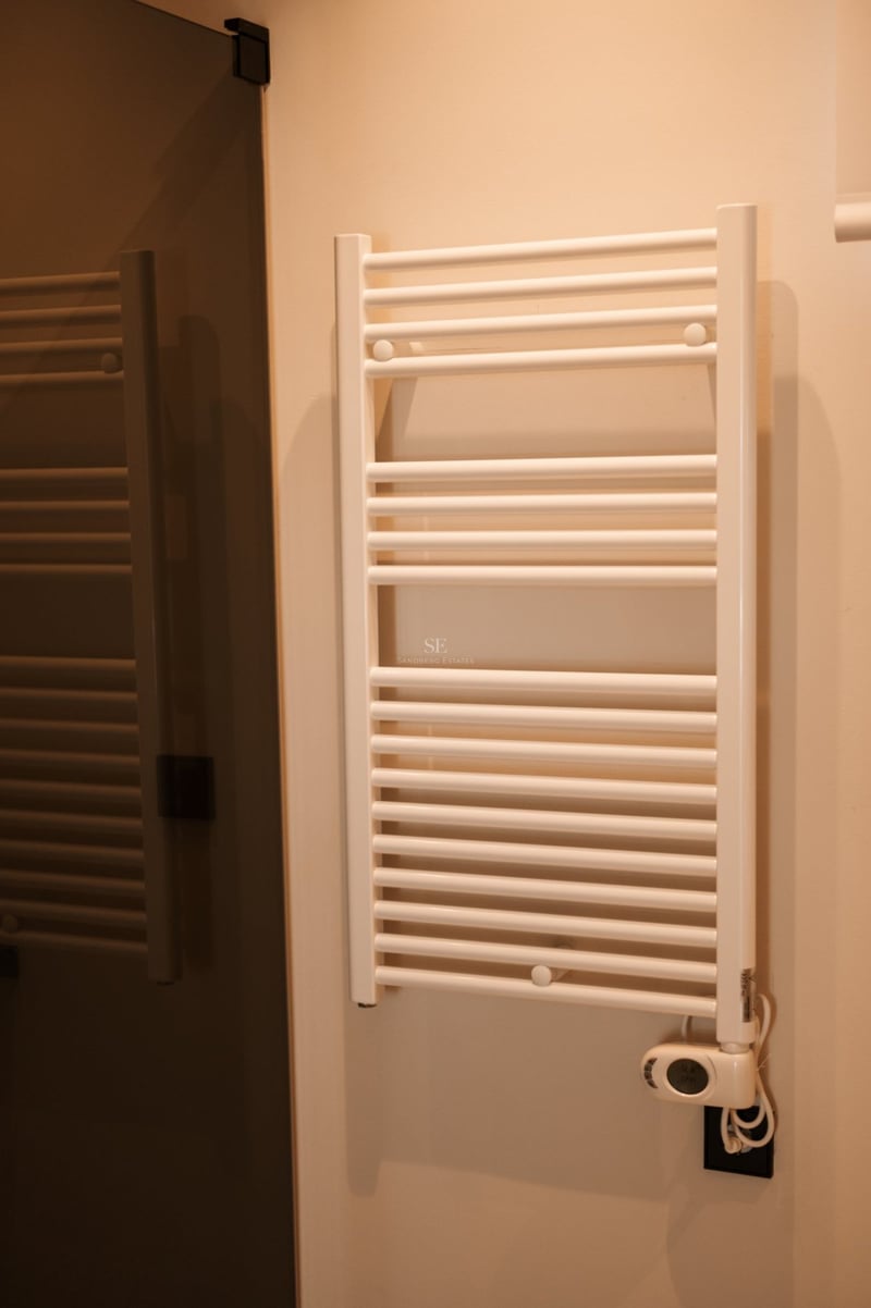 Vue rapprochée d'un radiateur sèche-serviettes blanc fixé sur un mur de couleur crème dans une salle d'eau.