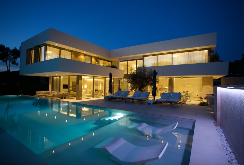 Villa blanche contemporaine à deux étages au crépuscule avec grande piscine éclairée et chaises longues.