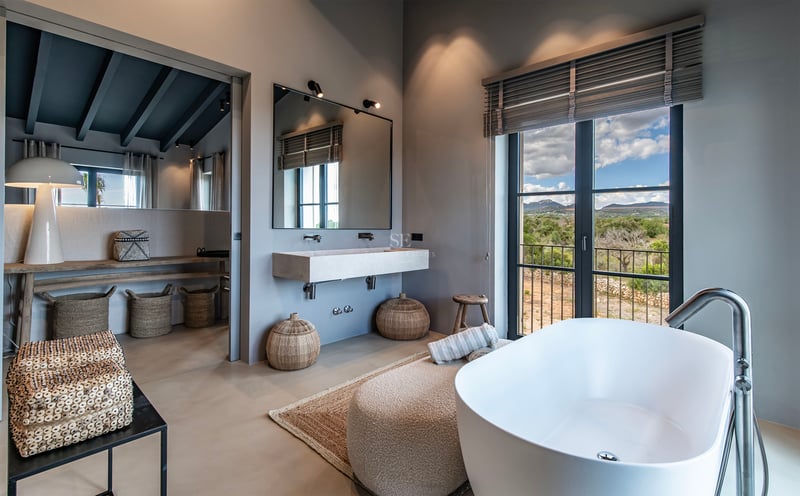 Salle de bain moderne avec baignoire îlot, lavabo suspendu et grande fenêtre donnant sur un paysage de montagne.