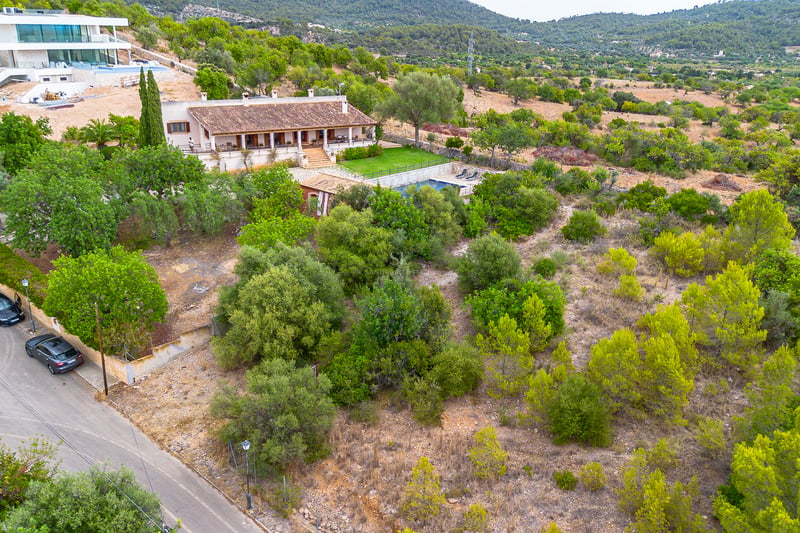 Vue aérienne d'une villa méditerranéenne rustique avec toit en terre cuite, piscine et jardin verdoyant sur les collines.