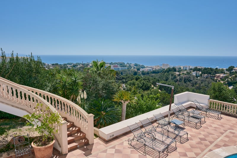 Terrasse en terre cuite avec chaises longues en fer forgé et escalier classique surplombant la mer.