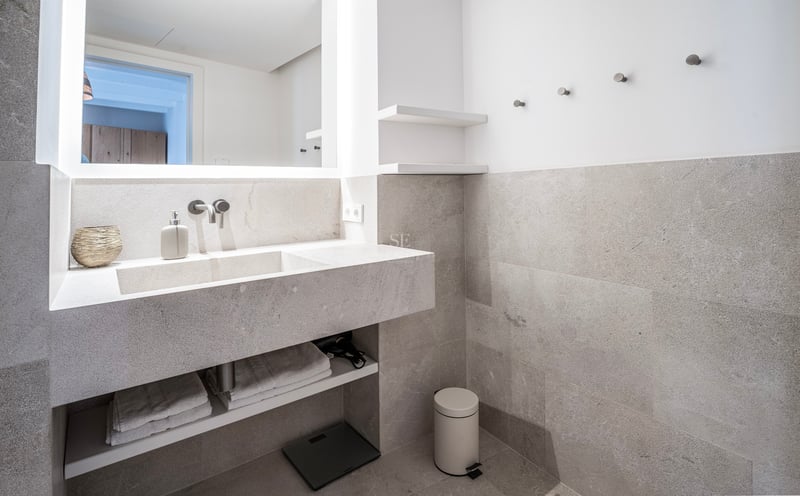 Salle de bain moderne avec vanité flottante en pierre grise, lavabo intégré et grand miroir rétroéclairé.