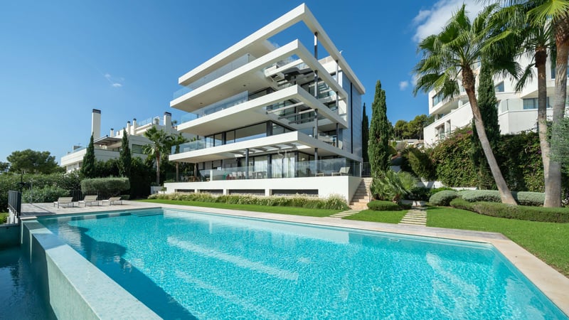Vue extérieure d'une villa moderne à plusieurs niveaux avec une grande piscine turquoise et un jardin paysager.