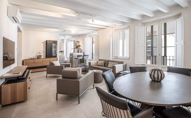 Élégant salon ouvert avec canapés gris, plafond à poutres blanches et lumière naturelle.
