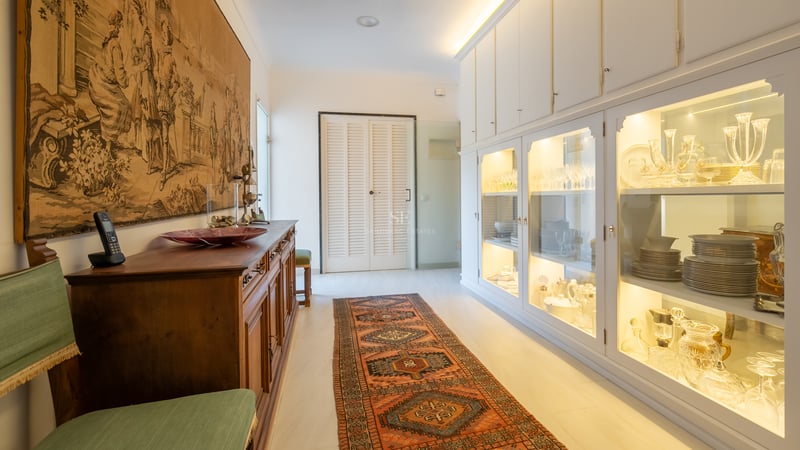 Couloir présentant une grande tapisserie historique, un tapis oriental et des vitrines blanches éclairées.