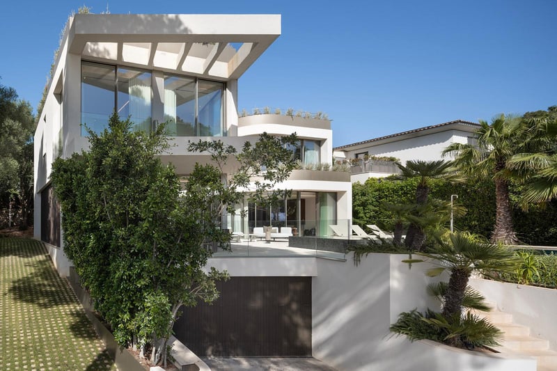 Façade d'une villa moderne blanche à plusieurs niveaux avec de grandes baies vitrées et des balcons en verre.