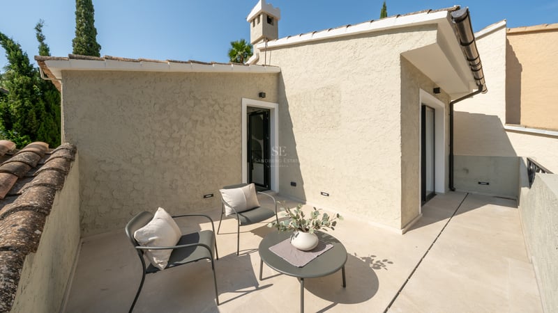 Terrasse ensoleillée avec deux chaises grises, une petite table et un sol en pierre beige.
