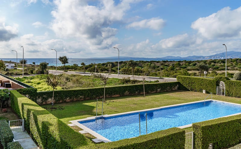 Piscine rectangulaire bleue entourée de pelouse et de haies avec la mer Méditerranée en arrière-plan.