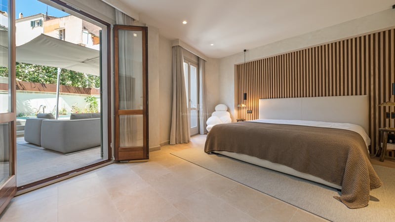 Chambre moderne avec mur en tasseaux de bois et grandes baies vitrées ouvrant sur un patio avec salon de jardin.