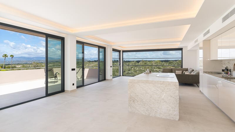 Espace de vie lumineux avec îlot en calcaire, baies vitrées toute hauteur et vue sur les montagnes.