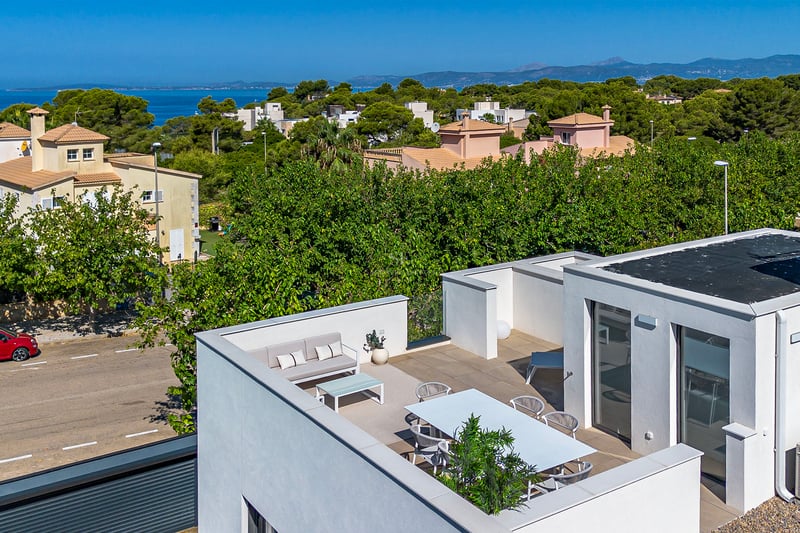 Modern vit takterrass med matplats och loungemöbler med utsikt över Medelhavet och pinjeträd.