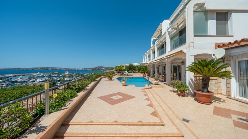 Grande terrasse extérieure avec piscine et vue sur un port de plaisance sous un ciel bleu.