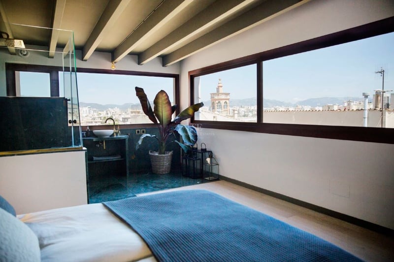 Dormitorio moderno con vigas de madera vistas, ventanales panorámicos y vistas a la catedral y la ciudad.