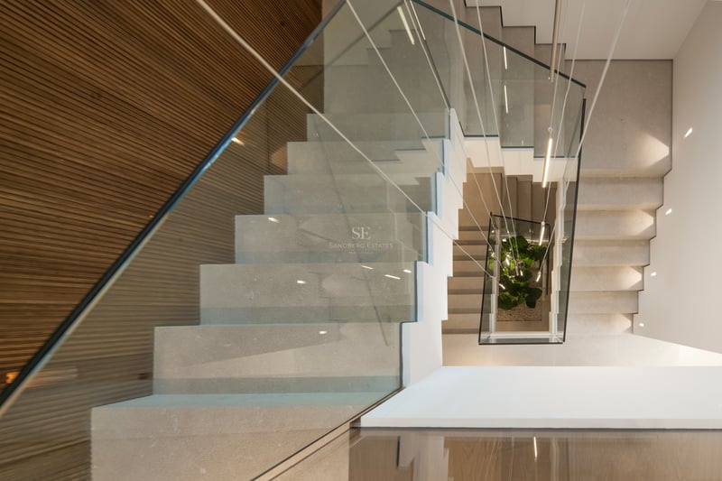 Vue de dessus d'un escalier moderne en pierre avec garde-corps en verre, mur en bois et luminaires suspendus.
