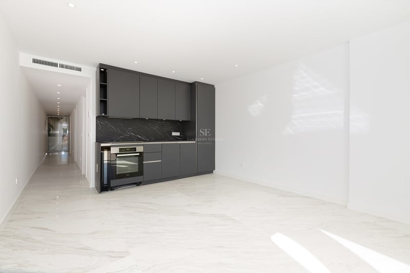 Espace cuisine moderne avec armoires gris foncé, crédence en marbre noir et sols en marbre blanc dans une pièce lumineuse.