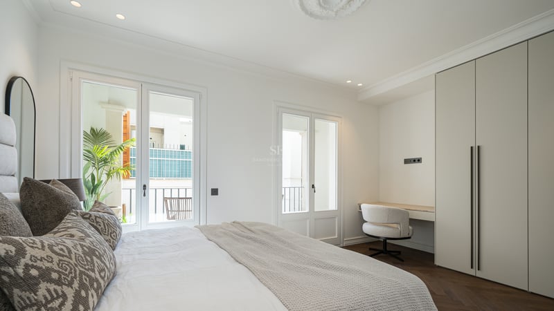 Spacious master bedroom featuring herringbone wood floors, built-in wardrobes, a desk, and French doors to a balcony.