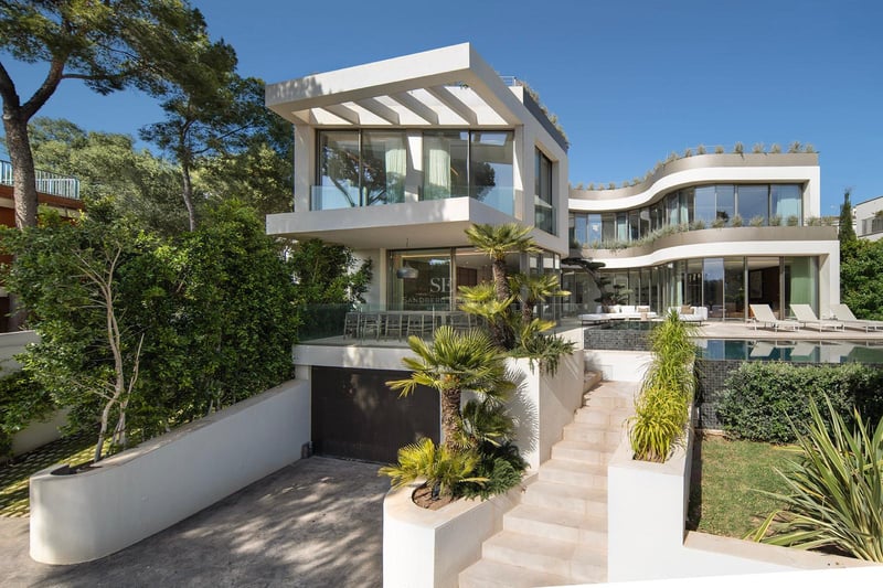 Villa moderne blanche à plusieurs niveaux avec façades vitrées courbes, piscine, palmiers et escalier en pierre.