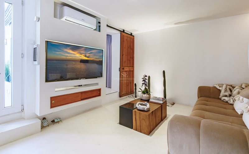 Salon blanc chaleureux avec télévision murale, grand canapé beige et porte de grange coulissante en bois.