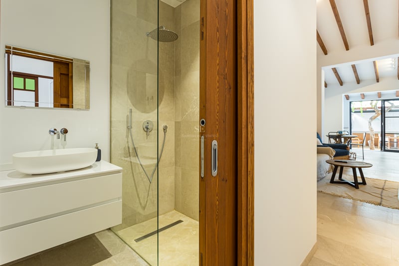 Salle de bain contemporaine avec douche en pierre, meuble vasque blanc et porte coulissante en bois.