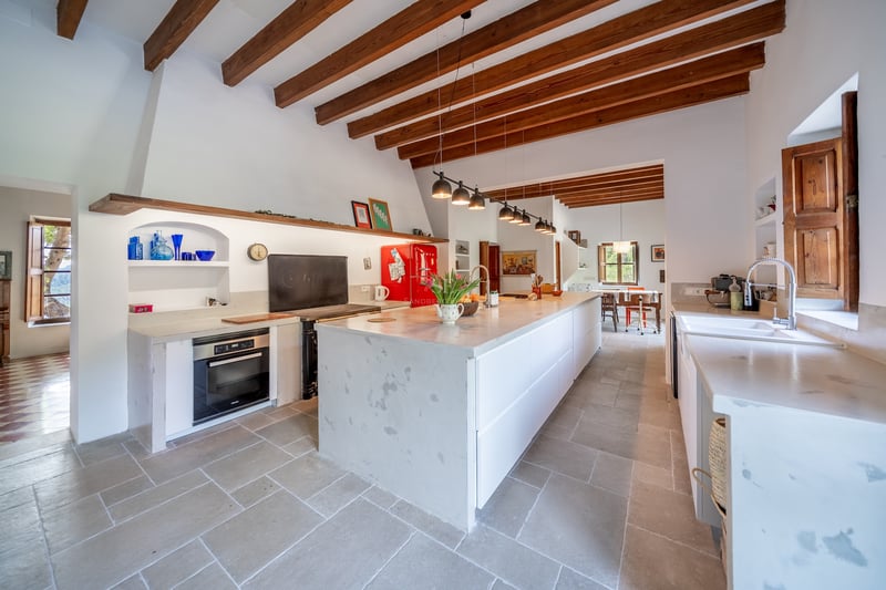 Cuisine spacieuse avec poutres en bois apparentes, grand îlot en pierre blanche et réfrigérateur rouge rétro.