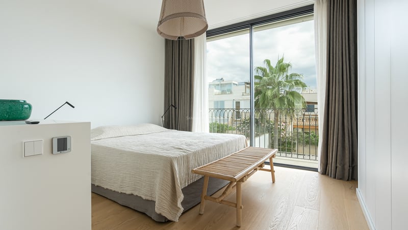 Chambre lumineuse avec baies vitrées, parquet en bois clair, grand lit et vue sur un palmier à l'extérieur.
