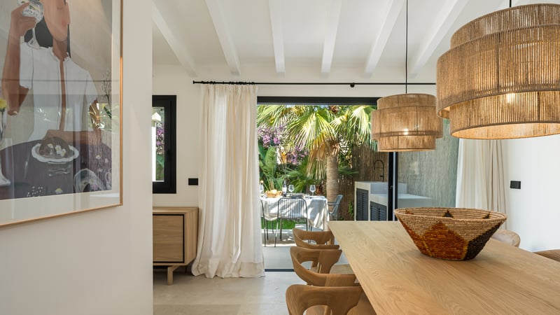 Salle à manger moderne avec table en chêne et suspensions en jute, s'ouvrant sur une terrasse de jardin luxuriante.