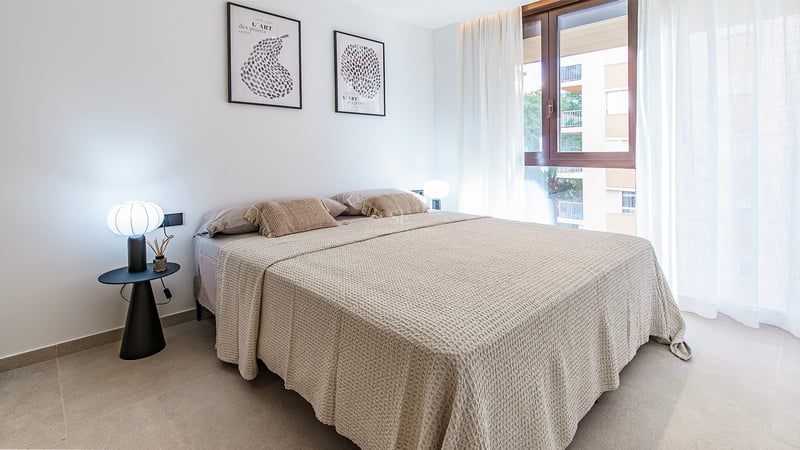 Chambre lumineuse avec grand lit, linge beige, lampes design et fenêtre avec rideaux voilages.