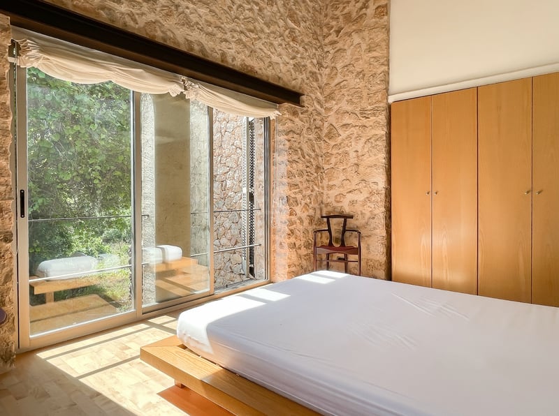 Chambre avec murs en pierre apparente, grandes baies vitrées coulissantes et placards intégrés en bois.