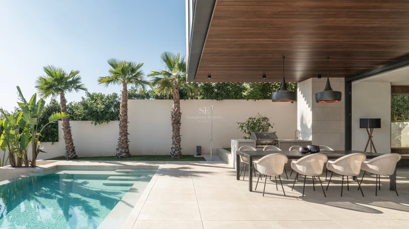 Terrasse moderne avec piscine turquoise, coin repas extérieur et plafond en bois avec suspensions design.