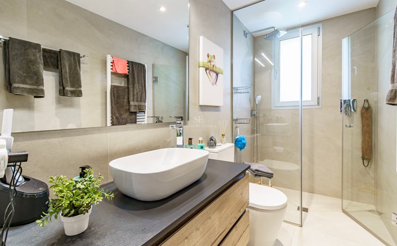 Salle de bain moderne avec vasque à poser blanche, douche vitrée et grand miroir.