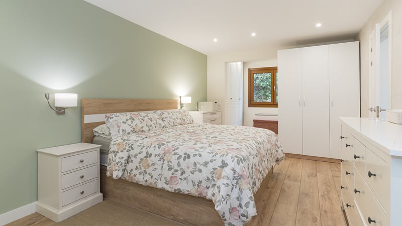 Chambre moderne avec lit floral, mur vert sauge, meubles blancs et parquet en bois clair.