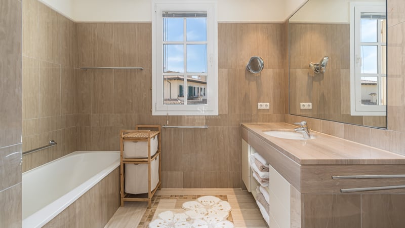 Salle de bain lumineuse avec baignoire, lavabo en pierre, grand miroir et fenêtre offrant une vue urbaine.